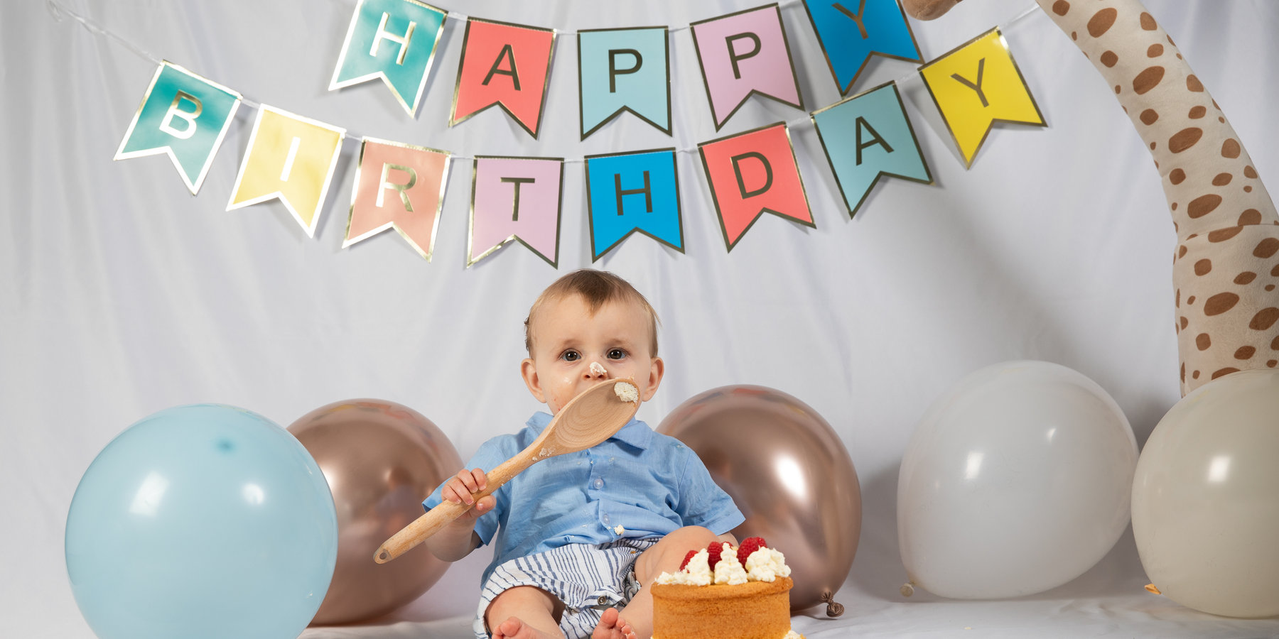 A baby sitting with a birthday cake beneath colourful bunting