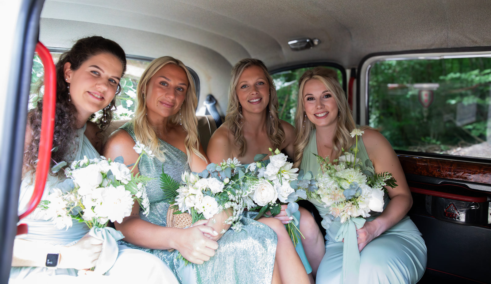 Four bridesmaids carrying bouquets inside a wedding car