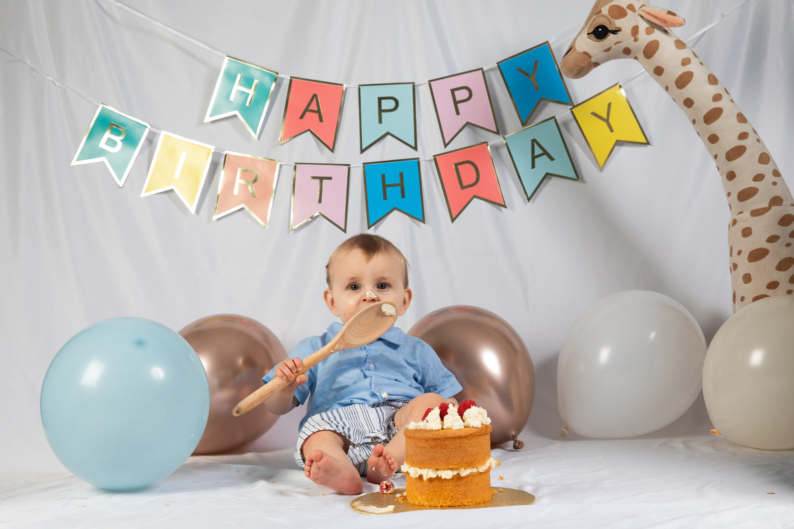 A baby sitting with a birthday cake beneath colourful bunting