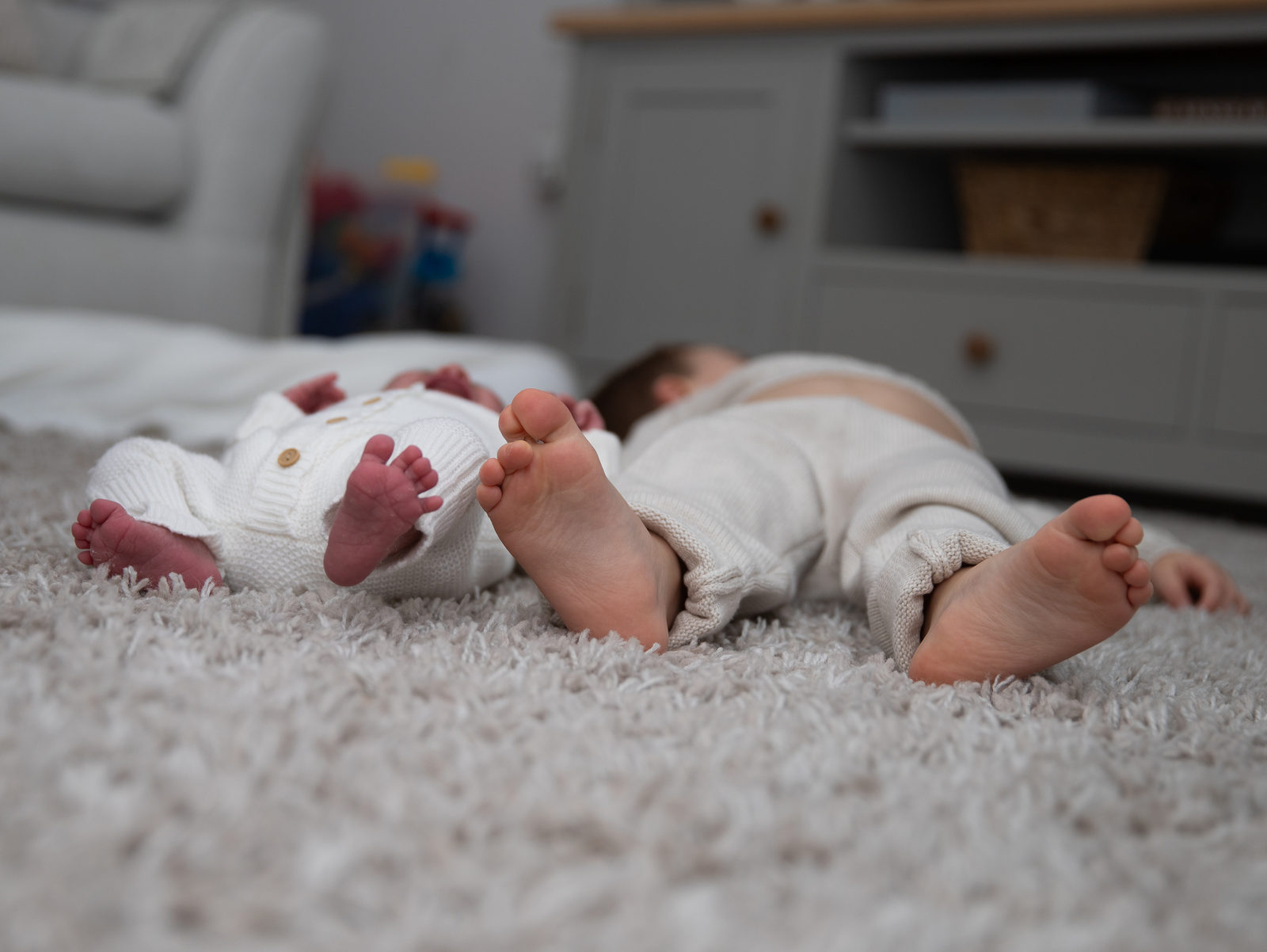 A newborn and older sibling lying together, photographed from their feet