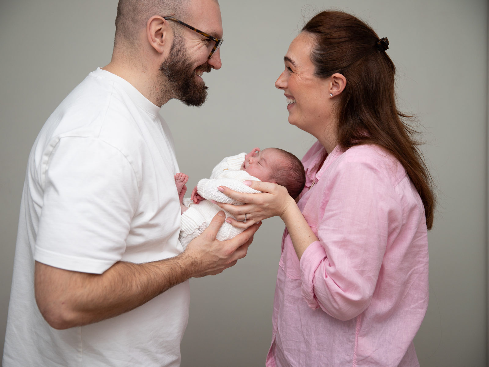 Two new parents smiling at one another while holding their baby