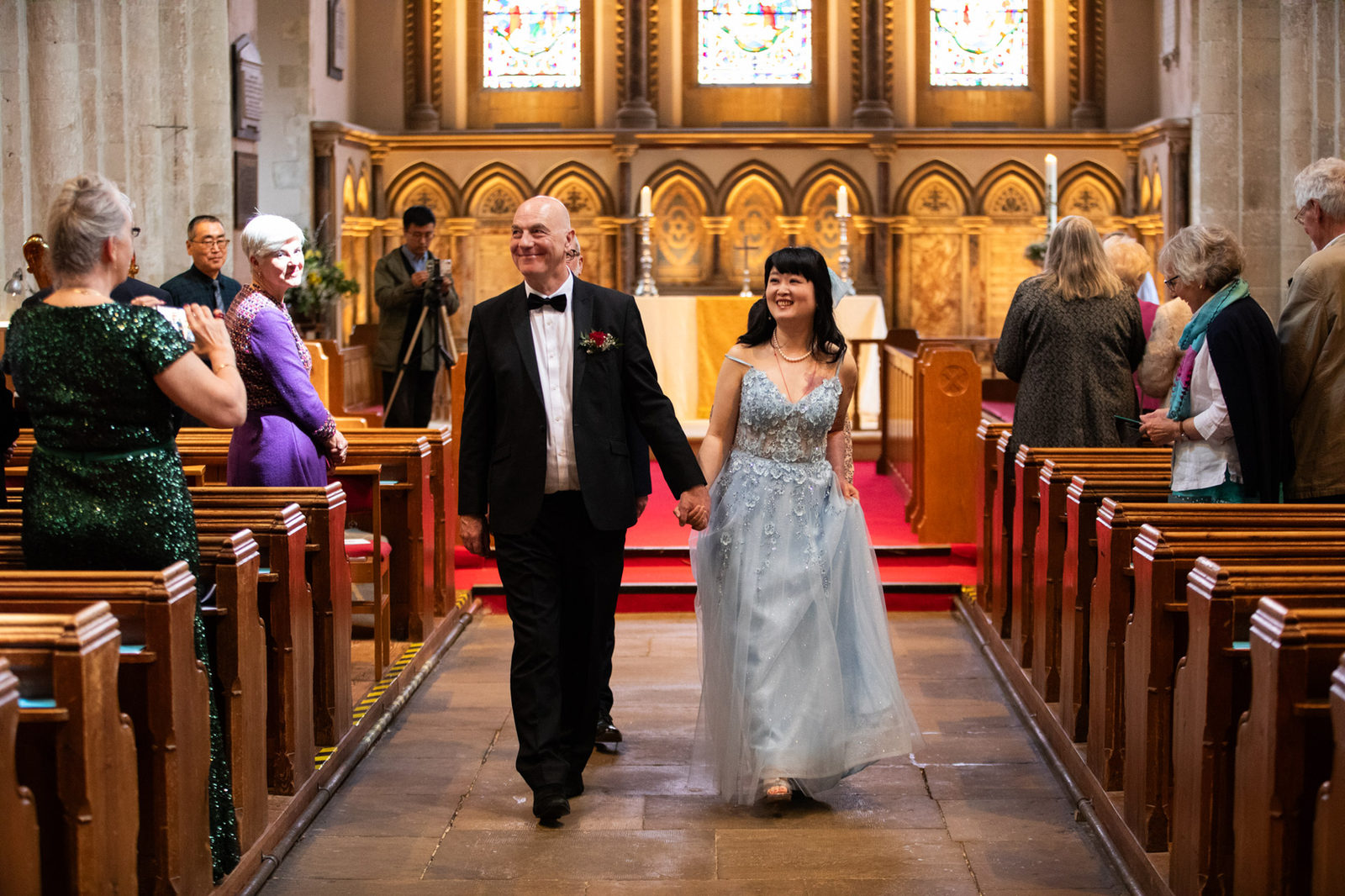 A newly married couple walking hand in hand down a church aisle