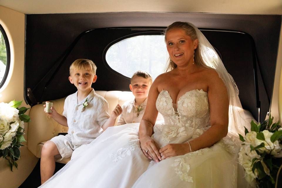 A bride and two young wedding attendants smiling inside a wedding car