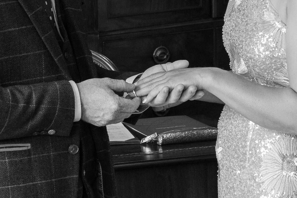 A black and white close-up of a couple exchanging wedding rings