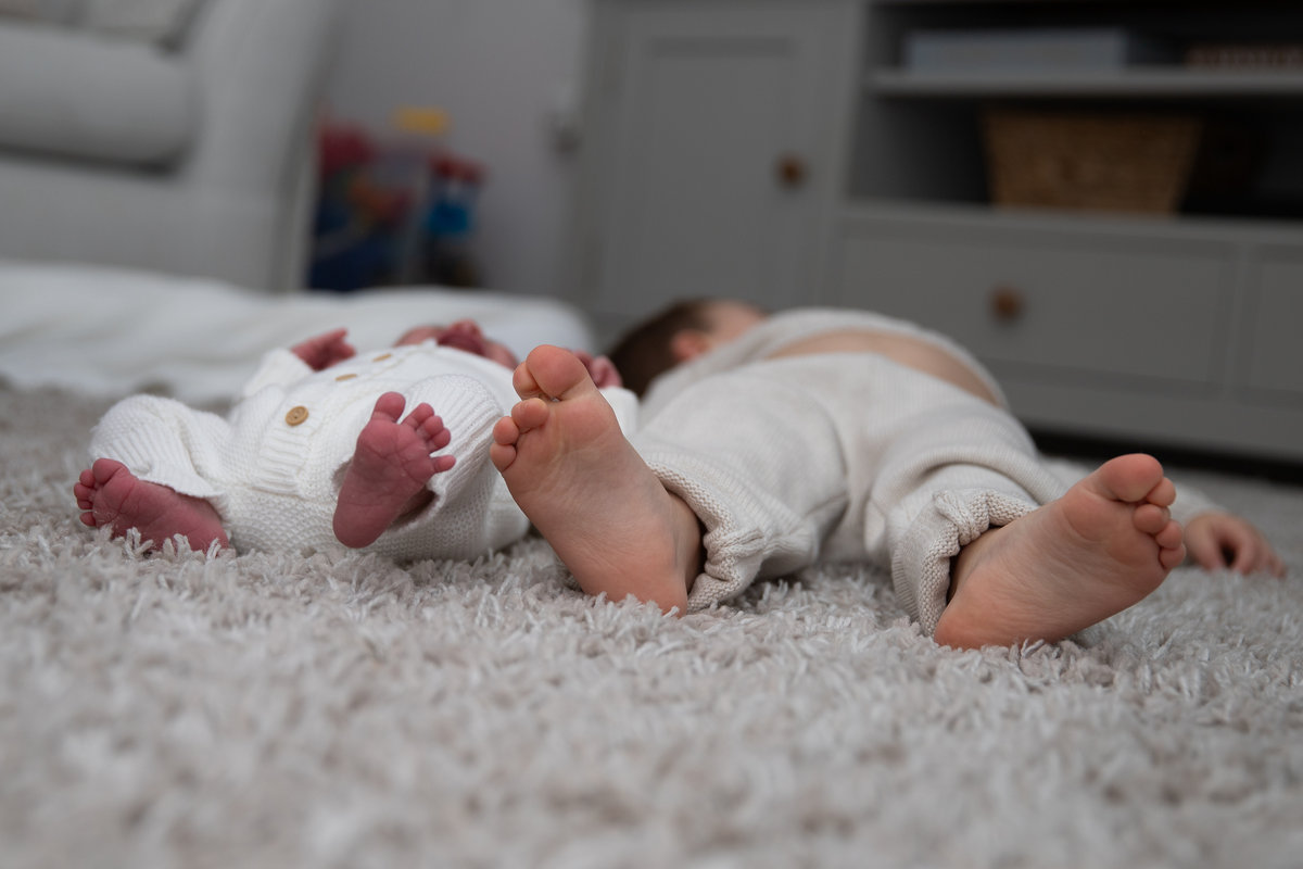 A newborn and older sibling lying together, photographed from their feet